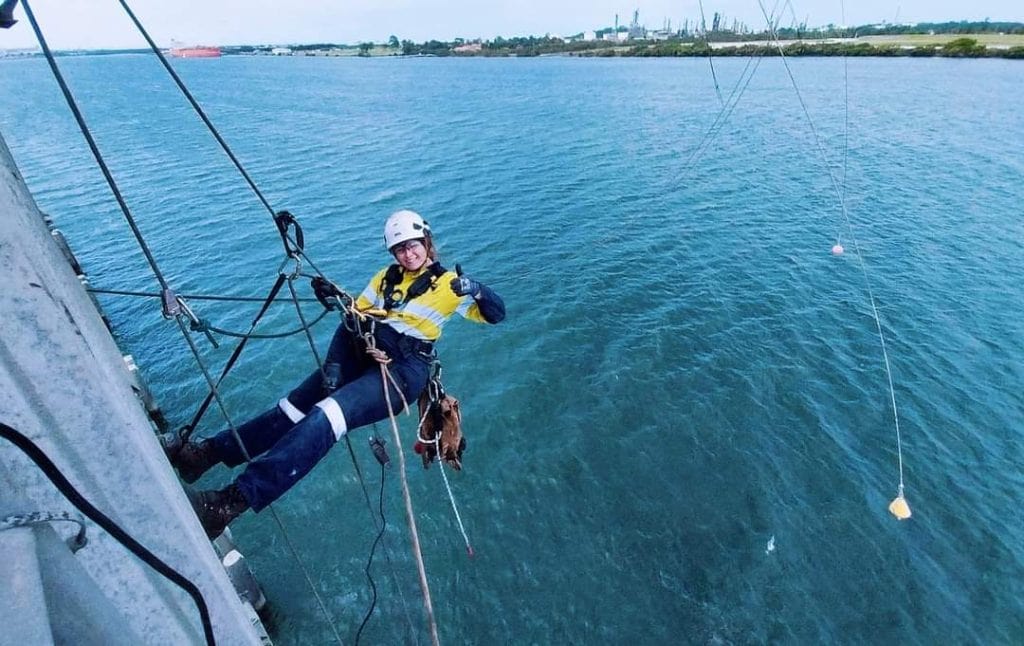 Rope access technician belaying over the ocean giving a thumbs up